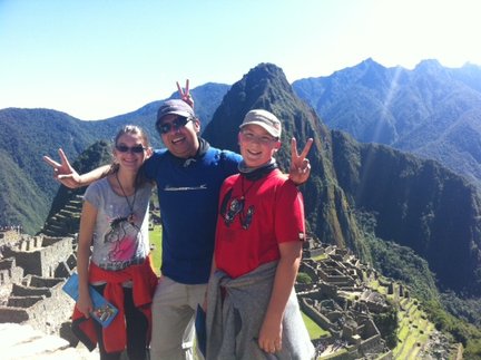 Drei fröhliche Personen posieren vor der beeindruckenden Kulisse von Machu Picchu, umgeben von majestätischen Bergen.