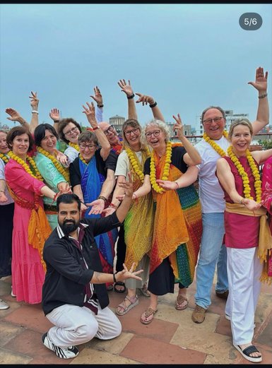 Eine Gruppe von Menschen in bunten Saris und mit Blumenketten posiert fröhlich für ein Foto während eines Tanzworkshops.