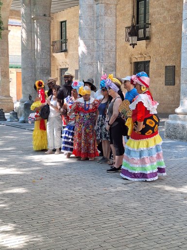 Eine Gruppe von Menschen in bunten traditionellen Kleidern posiert fröhlich unter einer Säulenarkade.