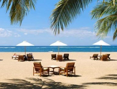 Ein sonniger Strand mit Liegen und Sonnenschirmen, umgeben von Palmen und dem klaren blauen Wasser des Ozeans.