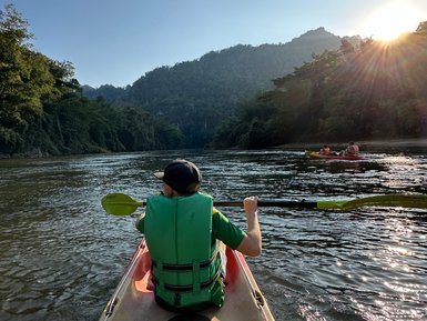 Junge paddelt in Kanu auf ruhigen Fluss in Kanchanaburi - Thailand mit Kindern