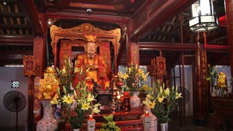 Ein prächtiger Altar mit einer Statue eines lächelnden Mannes, umgeben von bunten Blumen und traditionellen Dekorationen.