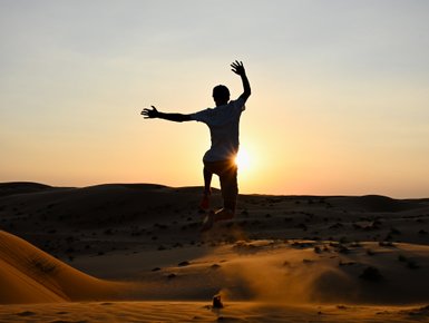 Silhouette eines Jungen beim Sonnenuntergang in der Wüste – Oman Reise mit Kindern