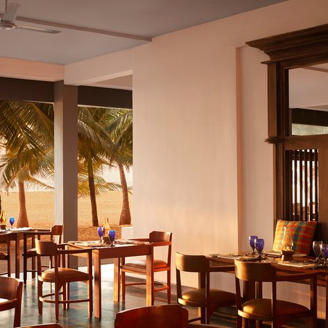 Ein elegantes Restaurant mit Holztischen und blauen Gläsern, umgeben von Palmen und einem Blick auf den Strand.