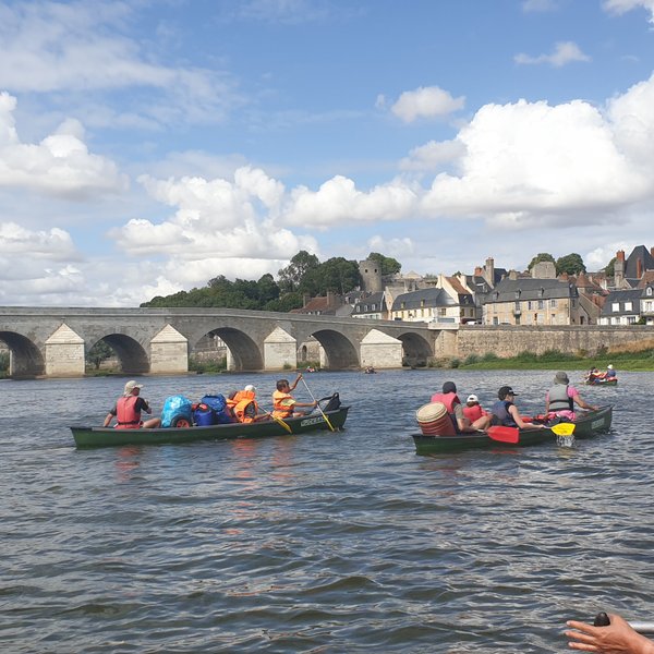 Eine Gruppe von Kanufahrern paddelt auf einem ruhigen Fluss, umgeben von einer malerischen Stadt und einer beeindruckenden Brücke.