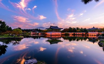 Ein malerischer Sonnenuntergang über dem Donggung Wolji Teich, mit reflektierenden Wolken und historischen Gebäuden im Hintergrund.