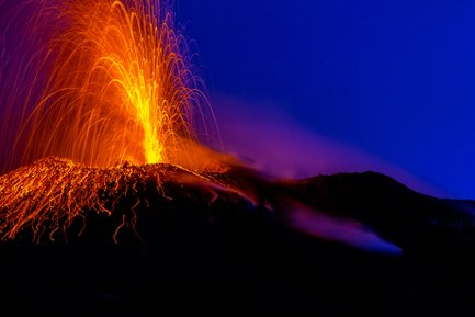Ein aktiver Vulkan spuckt glühende Lava und Asche in den Nachthimmel, während orangefarbene Funken aufsteigen.