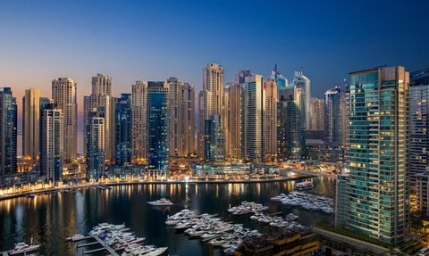 Die Skyline von Dubai bei Dämmerung, mit modernen Wolkenkratzern und einem ruhigen Yachthafen im Vordergrund.