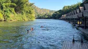 Kinder schwimmen an Floathouses am Flussufer in ruhiger Wasserlandschaft vorbei - Thailand mit Kindern