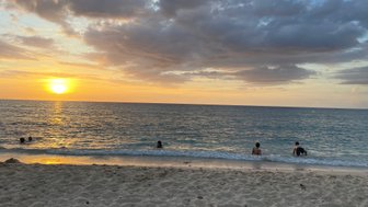 Ein Sonnenuntergang über dem Meer, während Menschen im Wasser planschen und die ruhige Atmosphäre genießen.