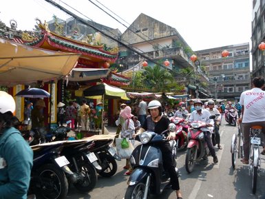 Eine belebte Straße in Saigon, gesäumt von Motorrädern und Menschen, die an einem sonnigen Tag unterwegs sind.