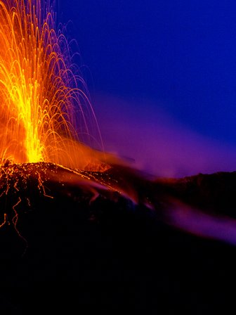 Ein aktiver Vulkan spuckt glühende Lava und Asche in den Nachthimmel, während orangefarbene Funken aufsteigen.