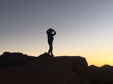 Eine Silhouette einer Person steht auf einem Felsen und blickt auf den Sonnenuntergang über den Bergen.