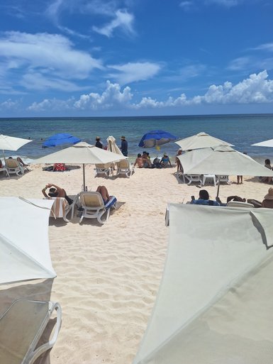 Am Strand von Playa del Carmen entspannen Menschen unter Sonnenschirmen, während die Wellen sanft ans Ufer plätschern.