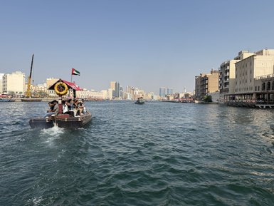 Eine traditionelle Dhow fährt auf dem Wasser, während Passagiere die Aussicht auf die moderne Skyline von Dubai genießen.
