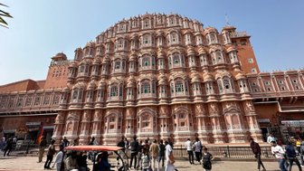 Das Hawa Mahal in Jaipur zeigt eine beeindruckende Fassade mit vielen Fenstern und kunstvollen Details, umgeben von Menschen.