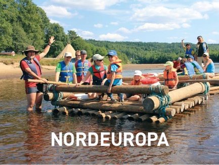 Eine Gruppe von Menschen auf einem Floß, das auf einem ruhigen Fluss schwimmt, umgeben von üppiger Natur und blauen Himmel.