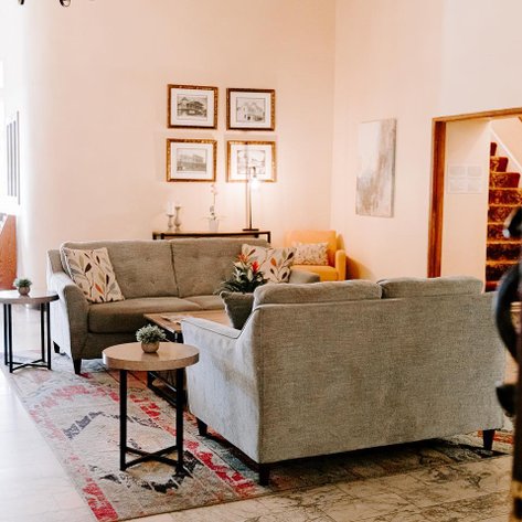 Ein einladender Lobbybereich mit grauen Sofas, kleinen Tischen und dekorativen Pflanzen, der Gemütlichkeit ausstrahlt.