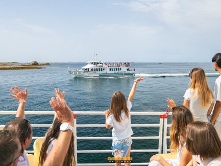 Eine Gruppe von Passagieren winkt einem Boot zu, das sanft über das Wasser gleitet, während die Sonne am Himmel scheint.