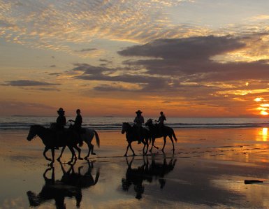 Reitergruppen genießen gemächlich den Sonnenuntergang am Strand, während sich der Himmel in warmen Farben färbt.
