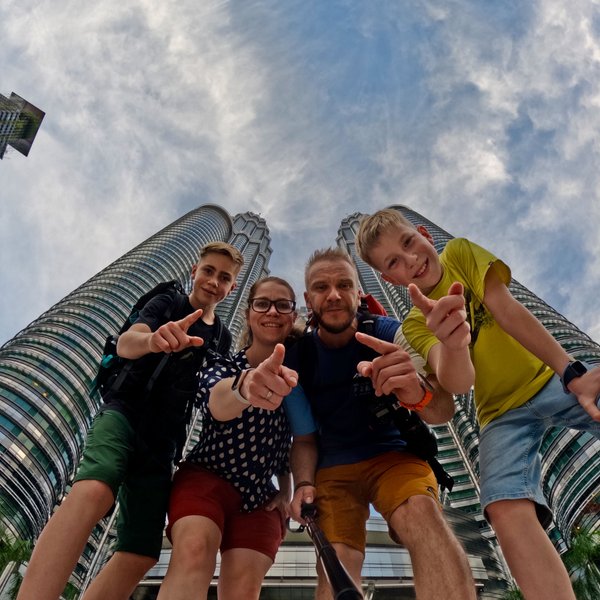 Familie posiert fröhlich für ein Selfie mit den Petronas Twin Towers im Hintergrund – Malaysia & Borneo Reise mit Kindern