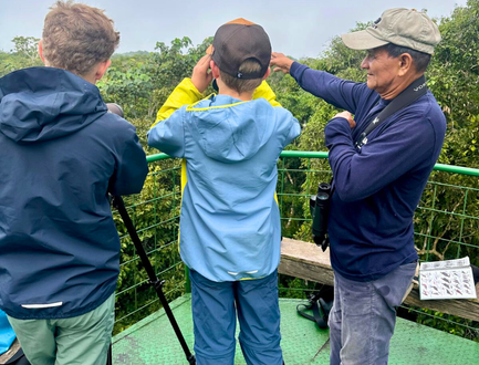 Drei Personen stehen auf einer Aussichtsplattform im Dschungel und beobachten die Umgebung mit Ferngläsern.
