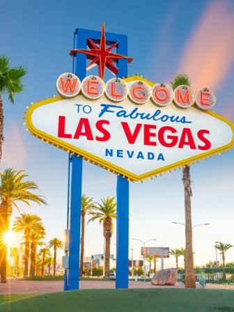 Das berühmte Willkommensschild von Las Vegas strahlt in leuchtenden Farben, umgeben von Palmen und einem klaren Himmel.