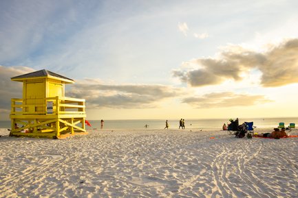 Ein leuchtend gelbes Rettungshaus steht am Strand, während Menschen im warmen Sonnenlicht spazieren gehen.