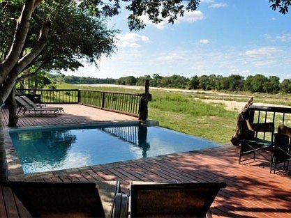 Ein einladender Pool auf einer Holzterrasse, umgeben von Bäumen und Blick auf eine weite, grüne Landschaft.