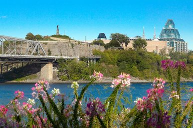 Eine malerische Aussicht auf den Fluss, umgeben von bunten Blumen und einer beeindruckenden Statue auf dem Hügel.
