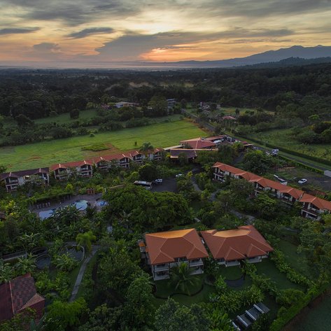 Eine Luftaufnahme eines Resorts mit roten Dächern, umgeben von üppigem Grün und einem Pool in der Mitte der Anlage.