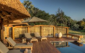 Eine entspannende Terrasse mit Liegen, einem Sonnenschirm und einem Pool, umgeben von üppiger Natur in Botswana.