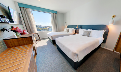 Ein modernes Hotelzimmer mit zwei Einzelbetten, großen Fenstern und einem Blick auf die Stadt Auckland.