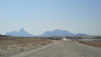 Eine unbefestigte Straße mit Bergen im Hintergrund - Namibia Familienurlaub