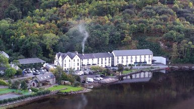 Ein malerisches Hotel am Ufer eines ruhigen Sees, umgeben von üppigem, grünem Wald und sanften Hügeln.
