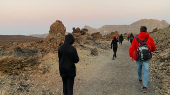 Eine Gruppe von Wanderern geht auf einem schmalen Pfad durch eine felsige Landschaft bei Dämmerung.
