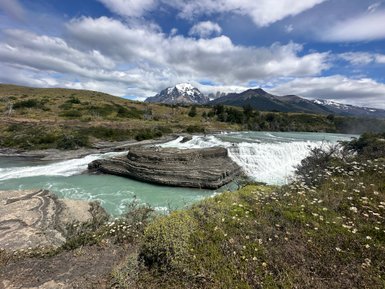 Ein beeindruckender Wasserfall stürzt über schichtige Felsen, umgeben von üppiger Vegetation und majestätischen Bergen im Hintergrund.