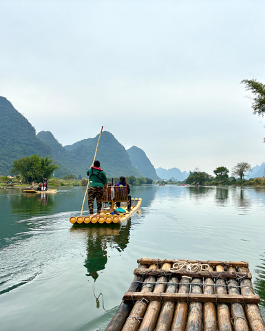 Eine Bambusflossfahrt auf einem ruhigen Fluss, umgeben von majestätischen Bergen und sanften Nebelschwaden.