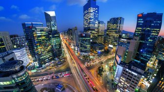 Die Stadt Seoul erstrahlt in der Dämmerung, mit leuchtenden Wolkenkratzern und lebhaften Straßen voller Autos.