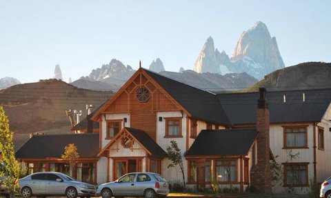 Ein charmantes Holzhaus mit einem großen Fenster, umgeben von majestätischen Bergen und klarem Himmel im Hintergrund.