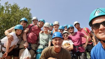 Eine Gruppe von Kletterern in blauen Helmen posiert fröhlich vor einer grünen Kulisse unter blauem Himmel.