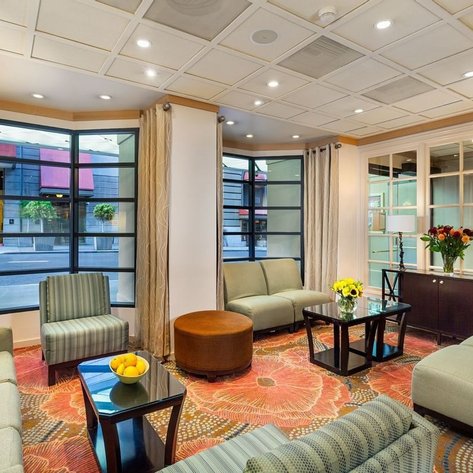 Ein eleganter Hotellobby mit bequemen Sofas, einem runden Tisch und einer großen Fensterfront, die auf die Straße blickt.