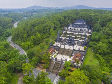 Eine beeindruckende Sicht auf das Kaisergrab von Khai Dinh, umgeben von üppigem Grün und sanften Hügeln im Hintergrund.