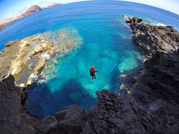 Ein Abenteurer springt von einer Klippe in das glitzernde, türkisfarbene Wasser vor der Küste Madeiras.