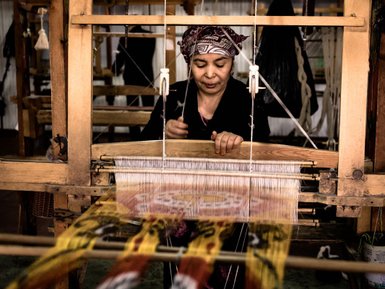 Eine Frau arbeitet konzentriert an einem Webstuhl und kreiert farbenfrohe Stoffe mit traditionellen Mustern.
