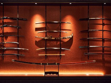 Eine beeindruckende Wand mit verschiedenen Katana-Schwertern, die kunstvoll auf einem orangefarbenen Hintergrund präsentiert werden.