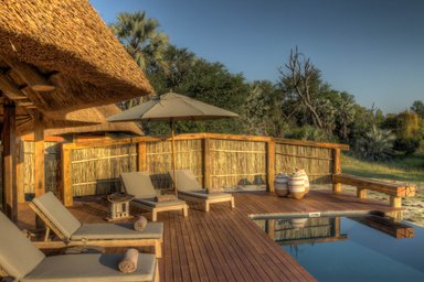Eine entspannende Terrasse mit Liegen, einem Sonnenschirm und einem Pool, umgeben von üppiger Natur in Botswana.