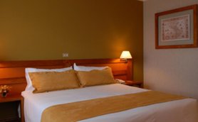 Ein gemütliches Hotelzimmer mit einem großen Bett, das mit beigen Kissen und einer Decke dekoriert ist.