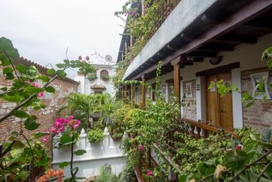 Ein malerischer Innenhof in Cartagena, umgeben von üppigem Grün und bunten Blumen, mit traditionellen Kolonialgebäuden im Hintergrund.