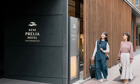 Zwei Frauen stehen vor dem Keio Prelia Hotel, lächelnd und mit Gepäck, bereit für ihren Aufenthalt in Kyoto.